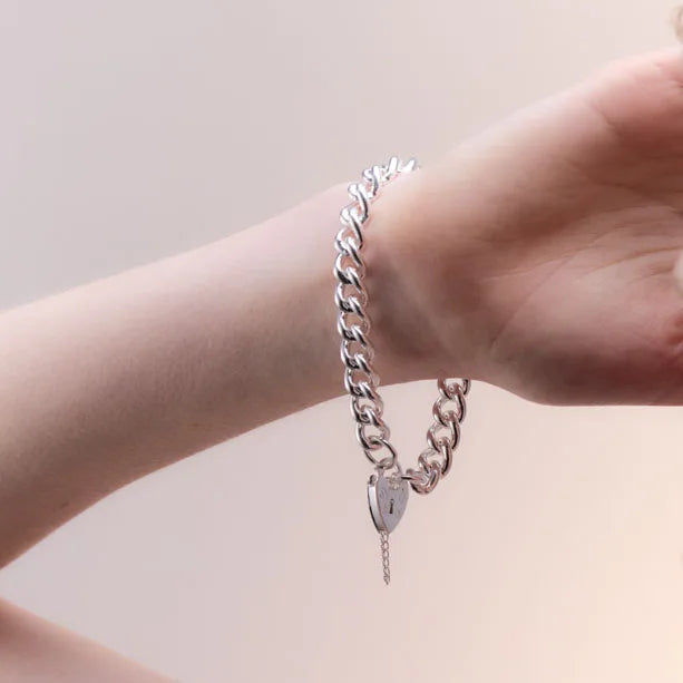 A sterling silver bracelet worn on the wrist, showcasing its comfortable 19 cm length and timeless design. The heart padlock adds a sentimental touch.