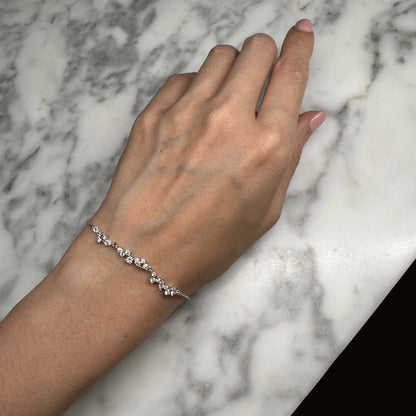 Elegant silver bracelet with a cascading design of sparkling cubic zirconia stones displayed on a woman's wrist against a marble background. The delicate and sophisticated piece is perfect for adding a touch of refinement to both everyday and formal outfits.