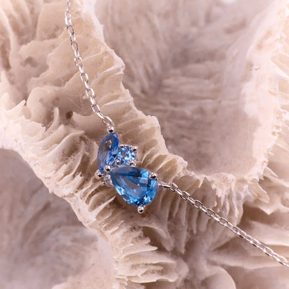 Sterling silver chain bracelet with striking blue topaz stones displayed on textured coral.