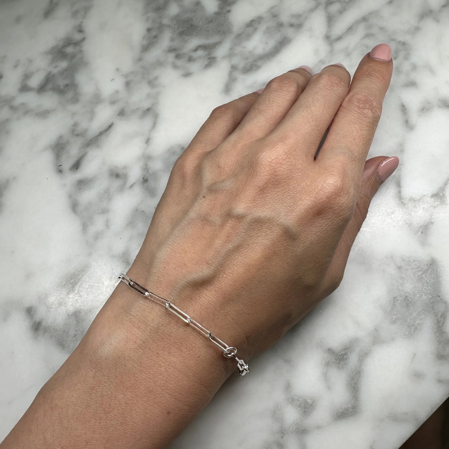 Close-up of a sterling silver oblong link bracelet on a wrist. Features a 17.5 cm length with a 2 cm extension, blending modern elegance with classic charm.