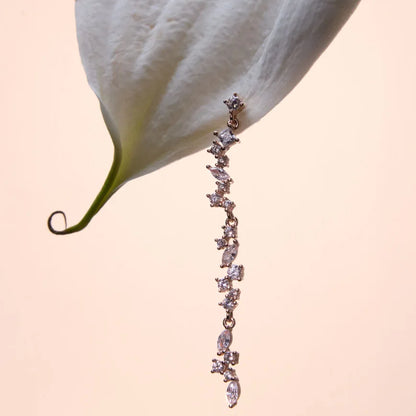 A single dangling cubic zirconia drop earring in rose gold displayed on a white lily, showcasing its graceful design and sparkling allure.