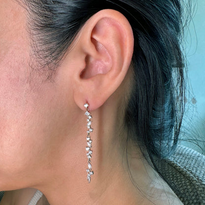 Close-up of a woman's ear wearing elegant long drop earrings with cascading cubic zirconia stones in a shimmering linear design. These lightweight, sparkling earrings add a touch of sophistication, perfect for formal occasions or creating a chic statement.