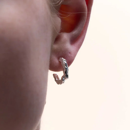 Close-up view of sterling silver textured half hoop earring worn on ear, showcasing its organic design and understated elegance.