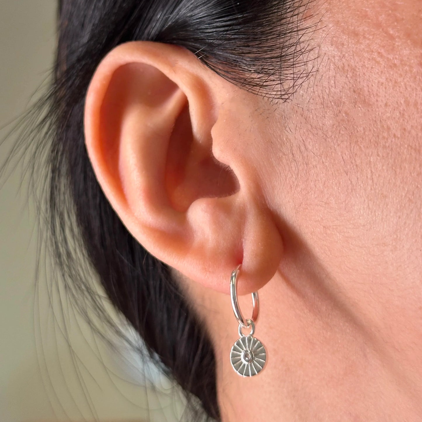 Close-up of a woman's ear wearing a sterling silver huggie earring with a radiant sun charm, offering a sleek and versatile accessory for day-to-night styling.