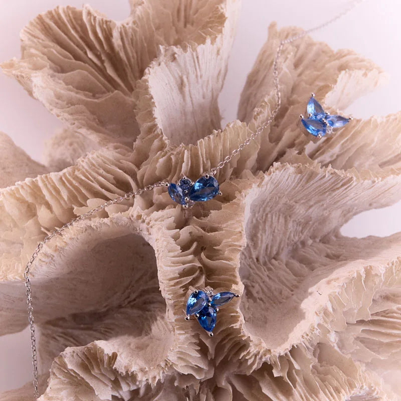 Exquisite sterling silver and blue topaz earrings, paired with matching jewellery, styled on a natural coral backdrop.