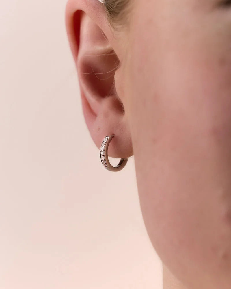 Close-up of a woman wearing a single 9k white gold huggie earring, featuring grain-set diamonds that add a touch of Australian elegance.