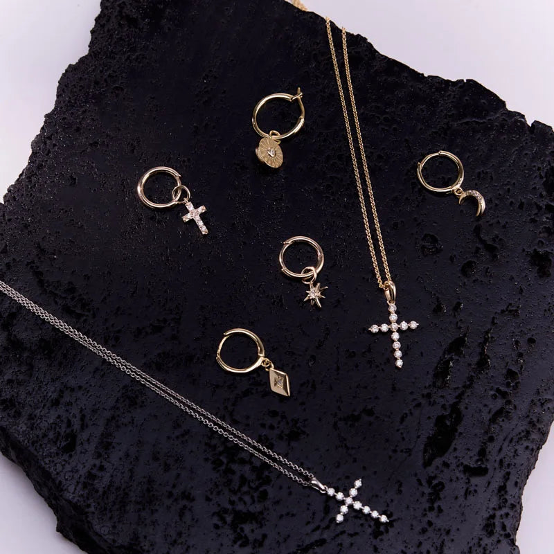 Jewellery collection featuring yellow gold plated accessories, including half hoop earrings with diamond-shaped charms, crosses, and star pendants, elegantly displayed.