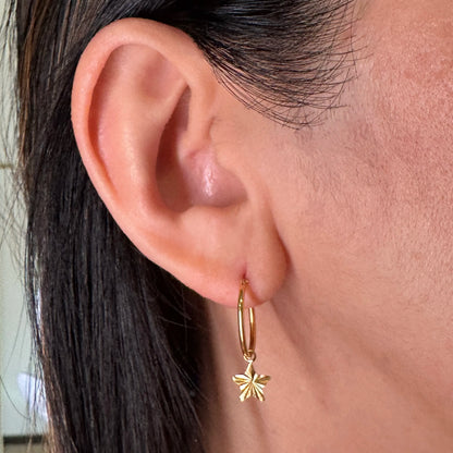 Close-up of a woman's ear featuring a sterling silver hoop earring with a delicate star charm, adding a minimalist yet chic touch to her outfit.