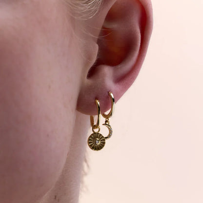 Close-up view of yellow gold plated crescent moon charm huggie earring adorned with cubic zirconia, elegantly worn on ear.