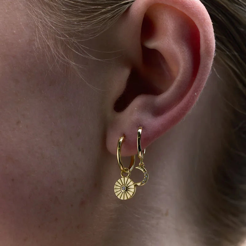 Detailed view of yellow gold plated star and crescent moon charm huggie earrings, showcasing celestial elegance with cubic zirconia accents.