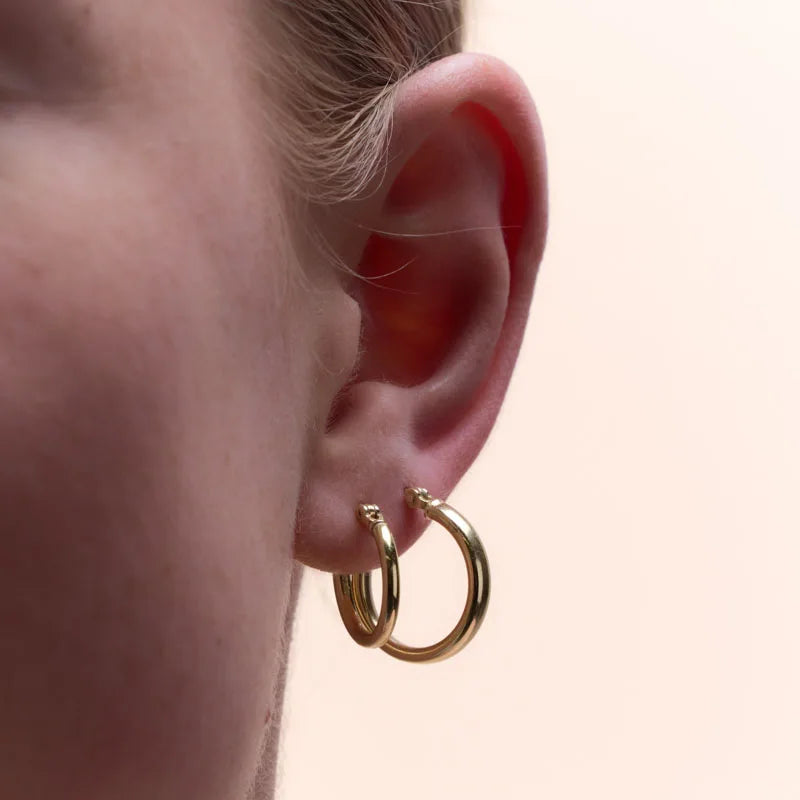 Close-up of yellow gold plated round tube hoop earrings worn, showcasing their sleek and sophisticated design.