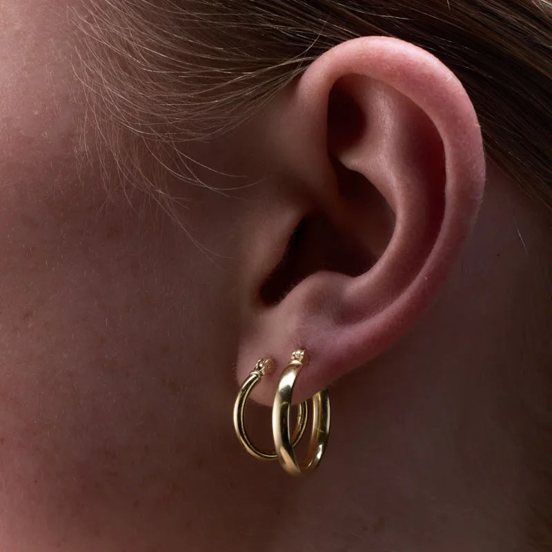 Yellow gold plated sterling silver round tube hoop earring elegantly displayed on a twig, emphasising its minimalist charm.