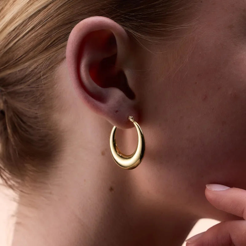 Close-up of a model wearing gold-plated tapered oval hoop earrings, highlighting their sophisticated design and lightweight comfort.