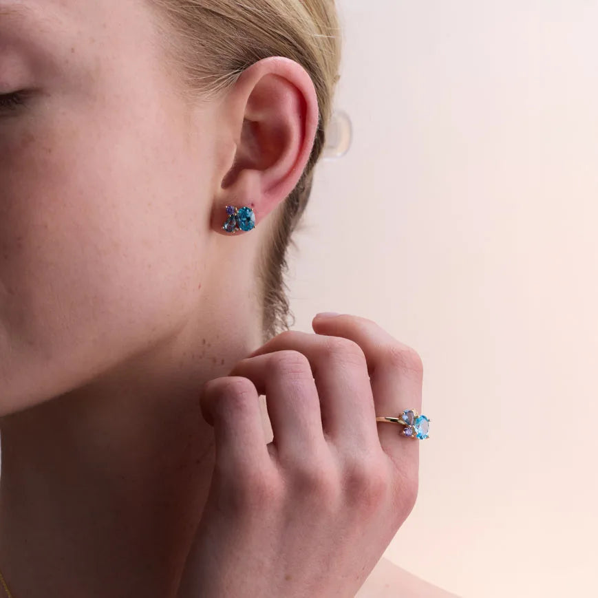 Close-up view of a woman's ear adorned with stunning yellow gold-plated earrings featuring blue topaz and amethyst gemstones for a radiant look.