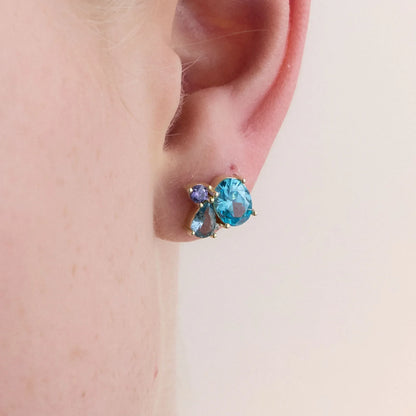 Detailed view of a single yellow gold-plated earring showcasing its brilliant gemstones, including blue topaz and amethyst, against a soft background.