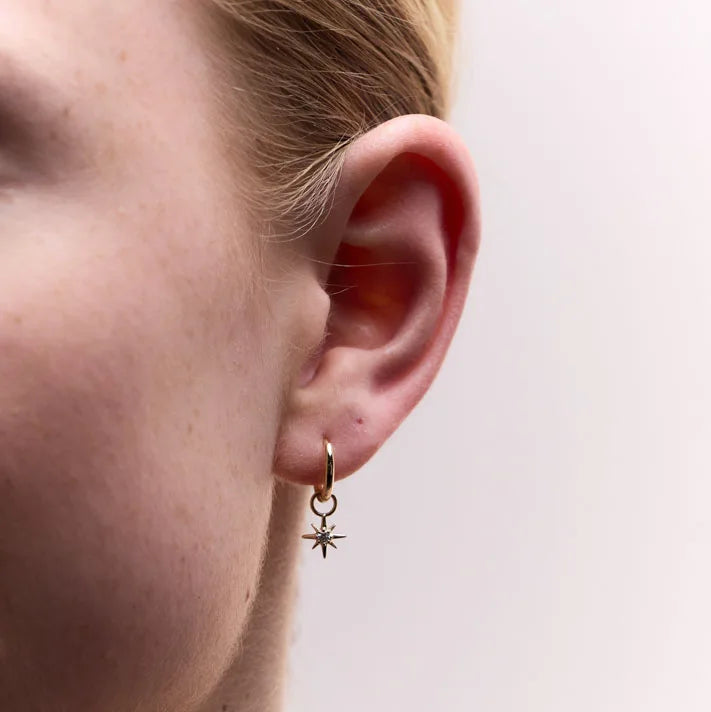 Close-up of 9k yellow gold hoop earrings with a star charm, elegantly worn, showcasing a versatile and chic design with brilliant diamond accents.