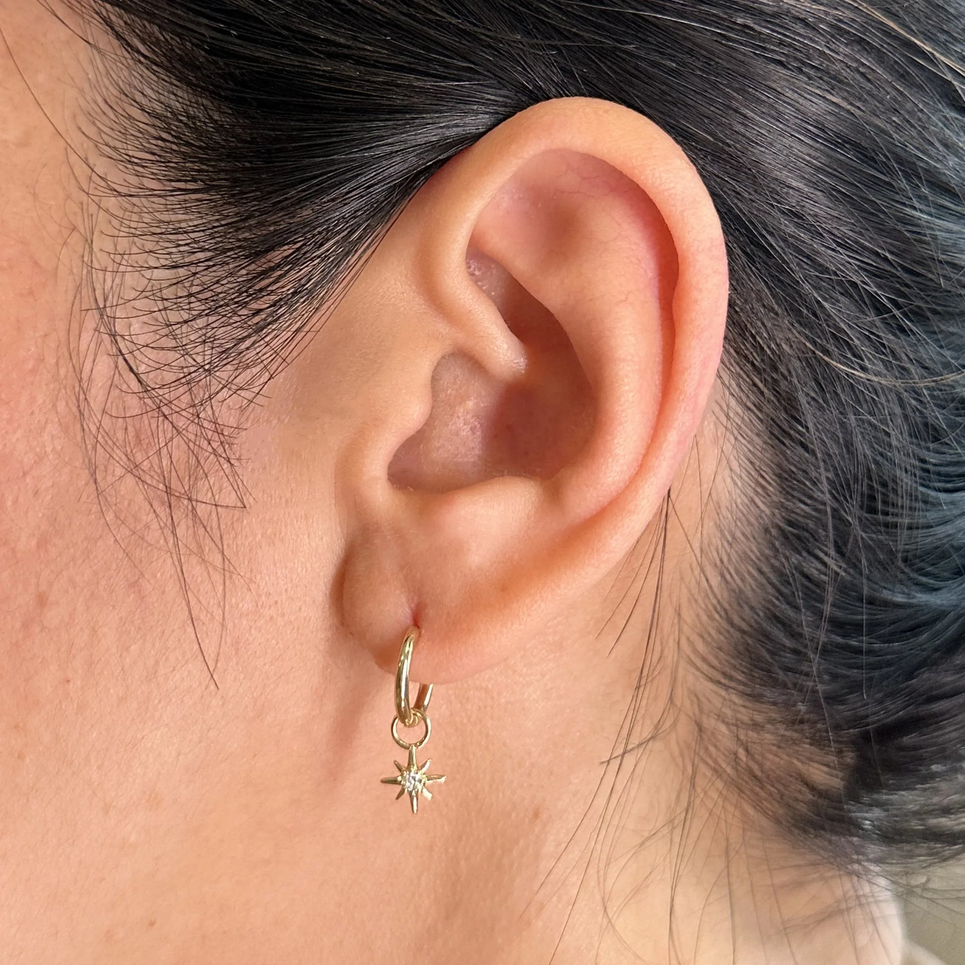 Close-up of a woman's ear wearing a minimalist yellow gold hoop earring featuring a delicate star charm with a sparkling diamond center. The lightweight and elegant design makes it perfect for everyday wear or layering with other earrings for a trendy, celestial-inspired look.