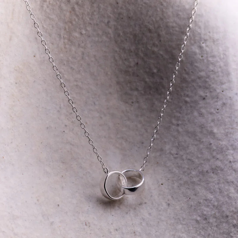 Minimalist sterling silver entwined circles pendant necklace displayed on a textured background, showcasing its sleek design and delicate craftsmanship.