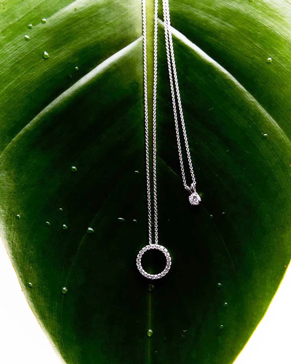 Diamond circle pendant with claw-set brilliance on a green leaf, emphasizing its contemporary elegance and light-catching design.