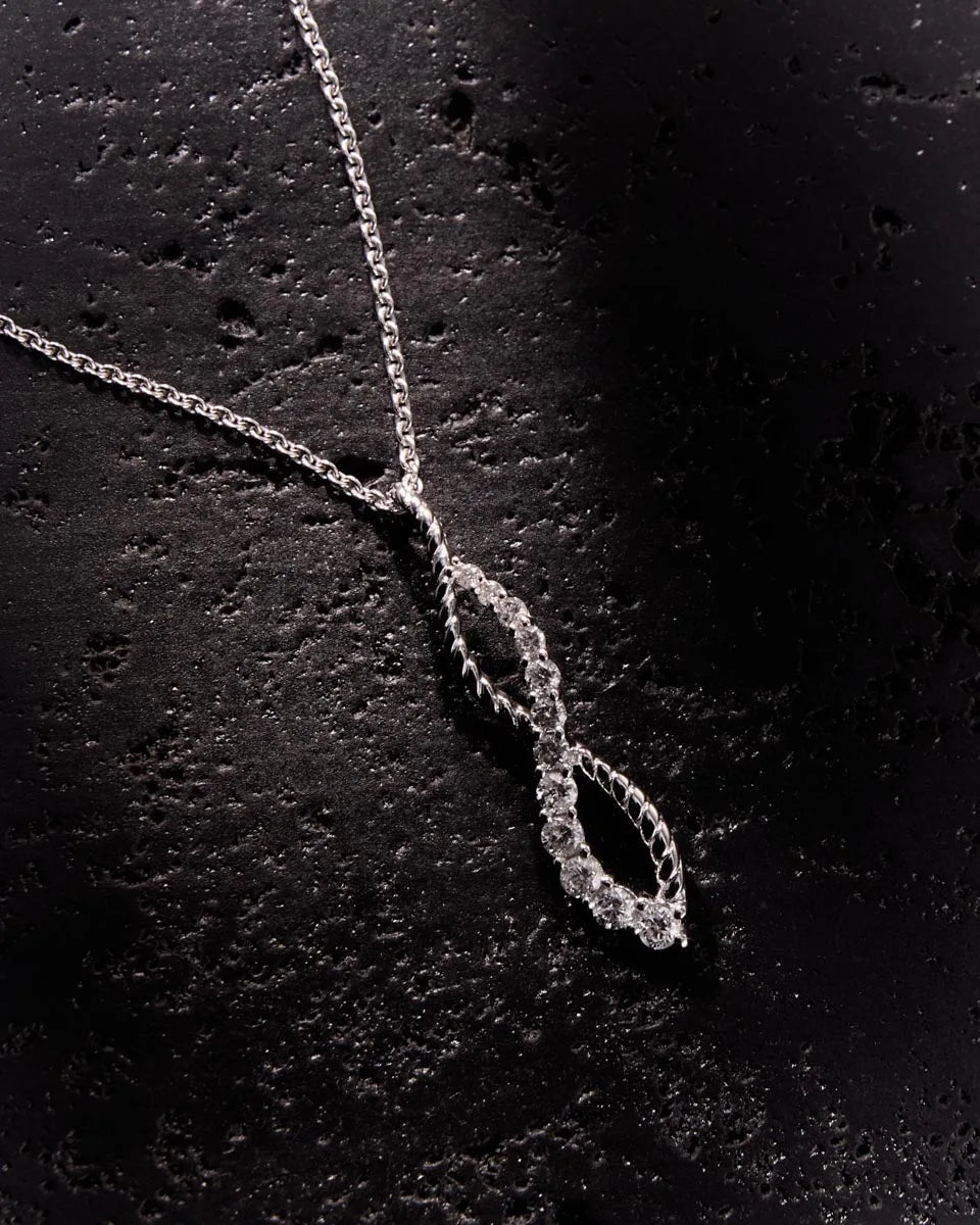 White gold infinity pendant adorned with 12 diamonds, showcasing a brilliant sparkle against a textured black surface for added sophistication.