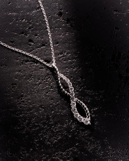 White gold infinity pendant adorned with 12 diamonds, showcasing a brilliant sparkle against a textured black surface for added sophistication.