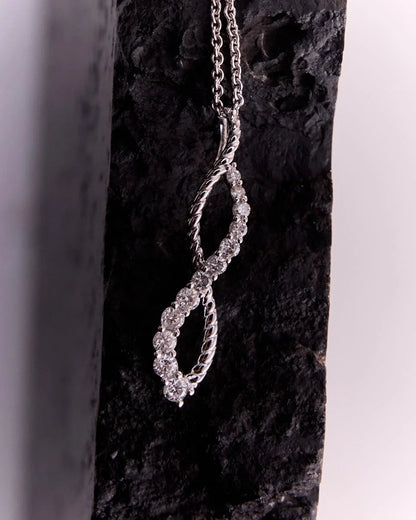 10k white gold infinity pendant with 12 diamonds totalling 0.25 carats, shown on a dark backdrop to highlight its elegant twisted design.