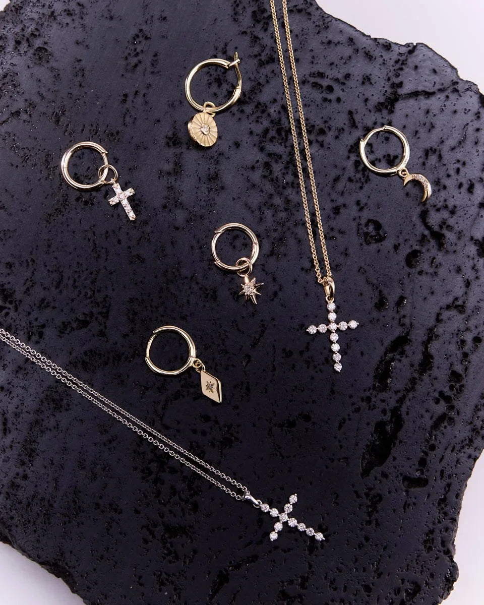 Jewellery collection featuring a diamond cross pendant in 9k yellow gold alongside coordinating designs, elegantly displayed on a textured surface.