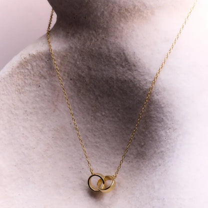 Gold-plated entwined circles pendant necklace displayed elegantly on a stone-like surface, symbolising lasting bonds and effortless sophistication.