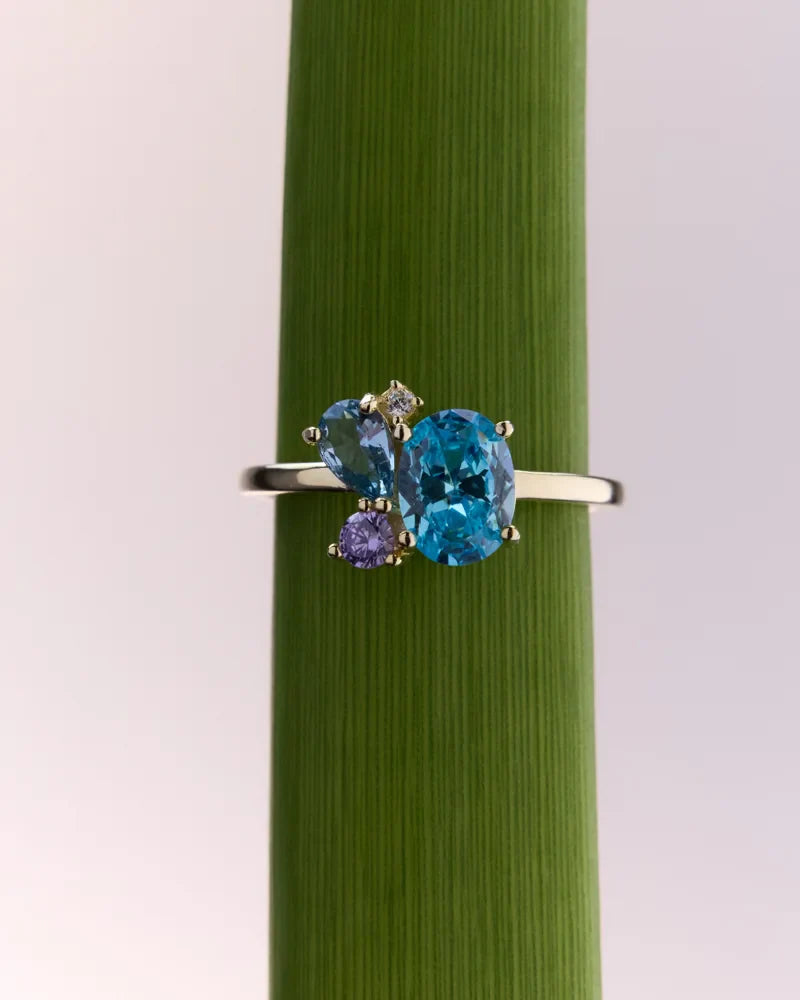 Gold-plated gemstone ring with London blue topaz and amethyst displayed on a green background, showcasing its vibrant colours and timeless style.